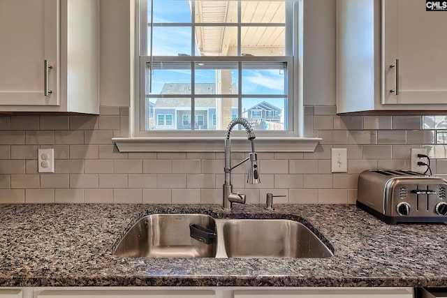 kitchen featuring backsplash, dark stone counters, sink, and white cabinets