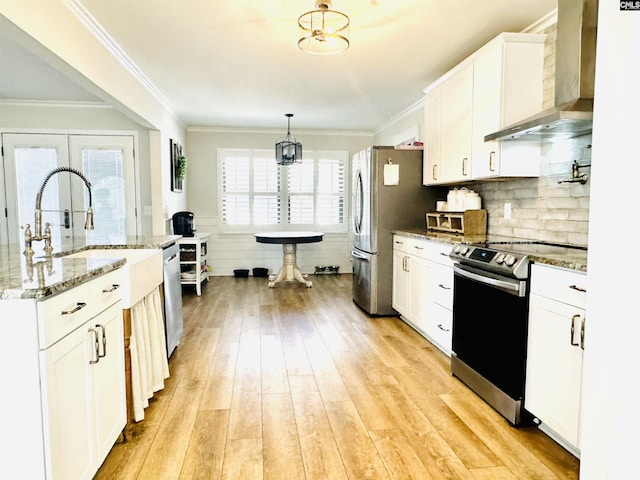 kitchen with wall chimney range hood, hanging light fixtures, stainless steel appliances, light hardwood / wood-style floors, and white cabinets