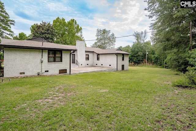 rear view of property featuring brick siding, a lawn, a chimney, crawl space, and a patio