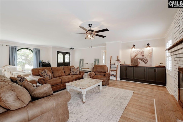 living room featuring a brick fireplace, crown molding, light hardwood / wood-style flooring, and ceiling fan