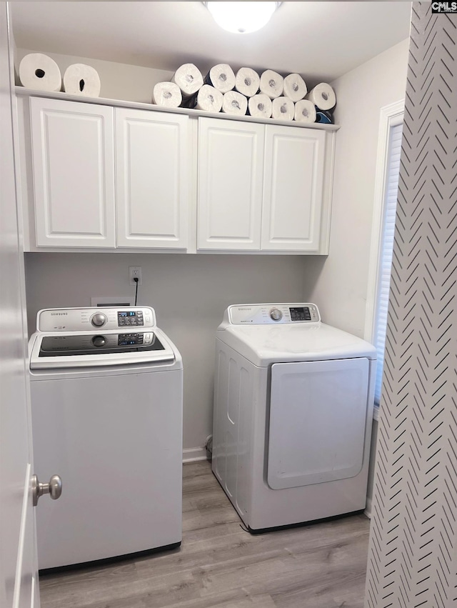 clothes washing area with cabinets, separate washer and dryer, and light wood-type flooring