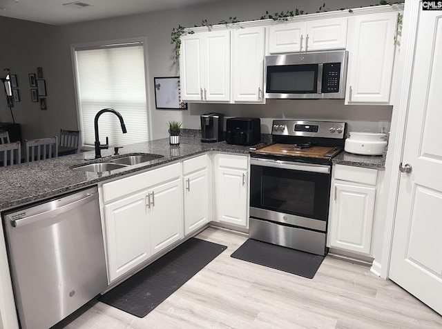 kitchen with sink, light wood-type flooring, dark stone countertops, appliances with stainless steel finishes, and white cabinets