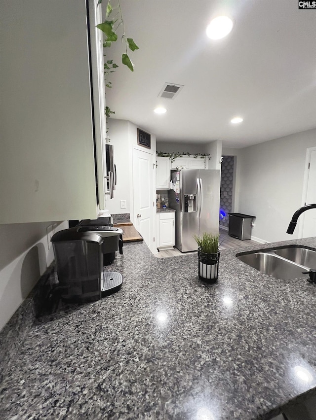 kitchen with white cabinets, sink, stainless steel fridge, and dark stone counters