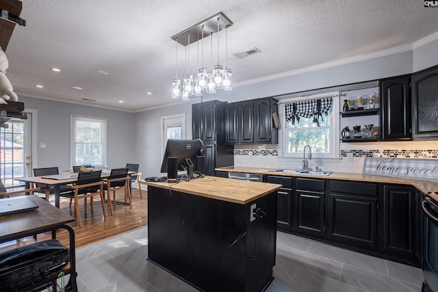 kitchen with pendant lighting, sink, decorative backsplash, a kitchen island with sink, and crown molding