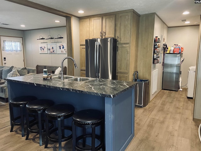 kitchen featuring sink, a breakfast bar area, stainless steel refrigerator, an island with sink, and light wood-type flooring