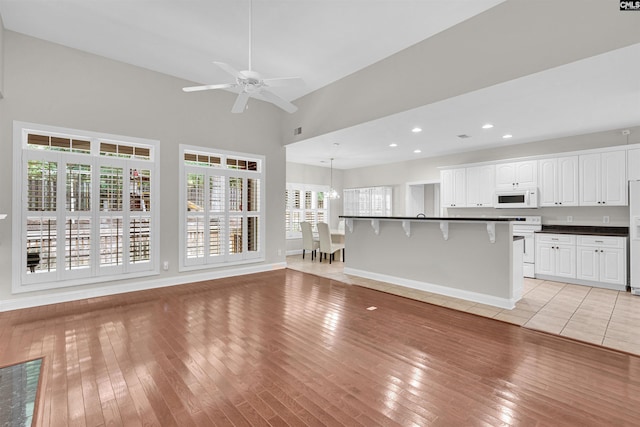 unfurnished living room with ceiling fan with notable chandelier, light hardwood / wood-style floors, and a high ceiling