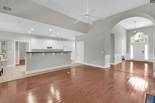 unfurnished living room featuring light hardwood / wood-style floors, ceiling fan, and a high ceiling