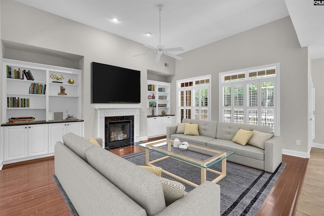 living room featuring hardwood / wood-style floors, built in shelves, a high end fireplace, and ceiling fan