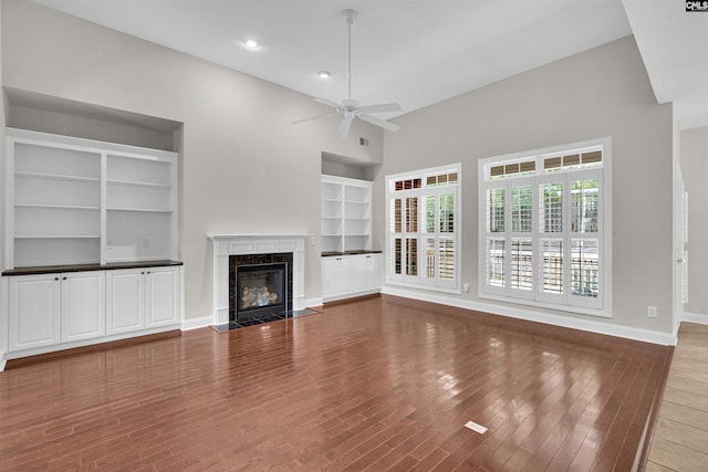 unfurnished living room featuring ceiling fan, hardwood / wood-style floors, built in features, and a high end fireplace