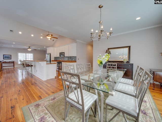 dining room featuring vaulted ceiling, ornamental molding, ceiling fan with notable chandelier, and light wood-type flooring