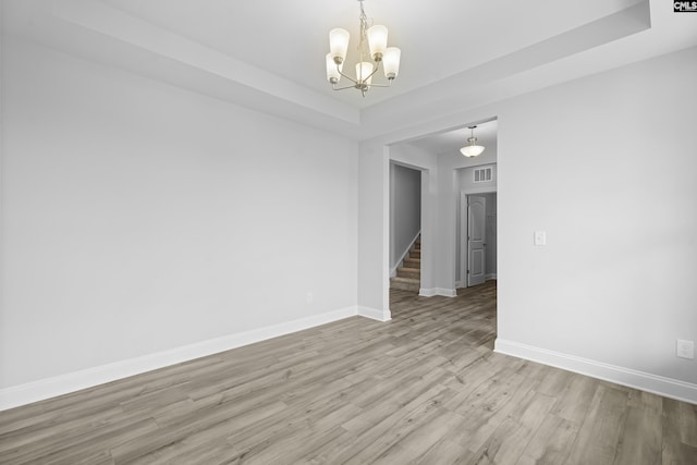 unfurnished room with an inviting chandelier, a tray ceiling, and light wood-type flooring