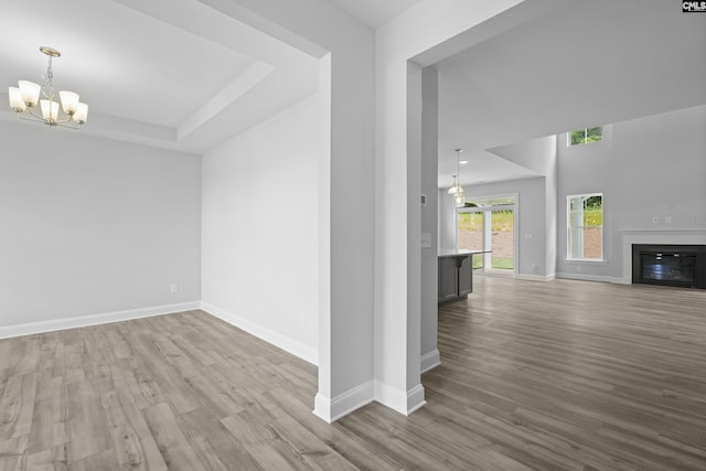 unfurnished living room with a notable chandelier, a raised ceiling, and light wood-type flooring