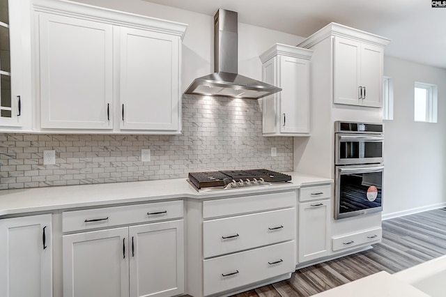 kitchen featuring stainless steel appliances, decorative backsplash, white cabinets, and wall chimney exhaust hood