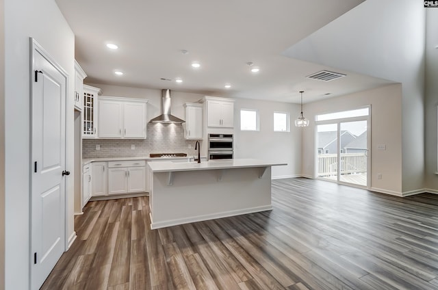 kitchen with dark hardwood / wood-style floors, tasteful backsplash, an island with sink, white cabinets, and wall chimney range hood