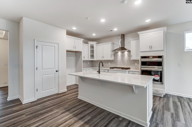 kitchen featuring white cabinetry, sink, a kitchen island with sink, stainless steel appliances, and wall chimney exhaust hood