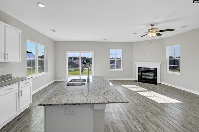 kitchen with light stone counters, a kitchen island with sink, sink, and white cabinets