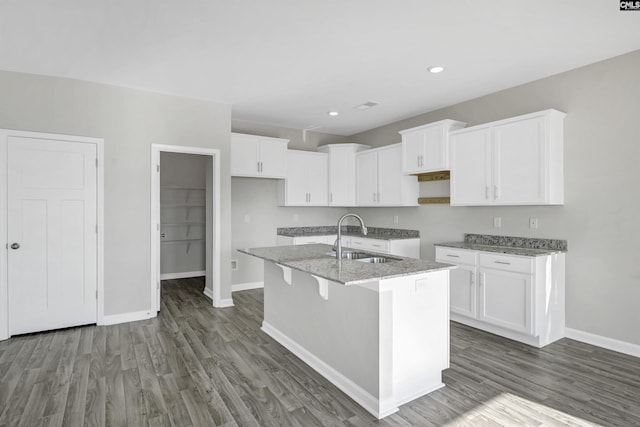 kitchen with an island with sink, stone countertops, sink, and white cabinets