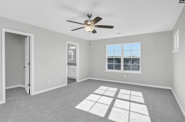 unfurnished bedroom featuring ceiling fan, a spacious closet, dark carpet, and ensuite bath