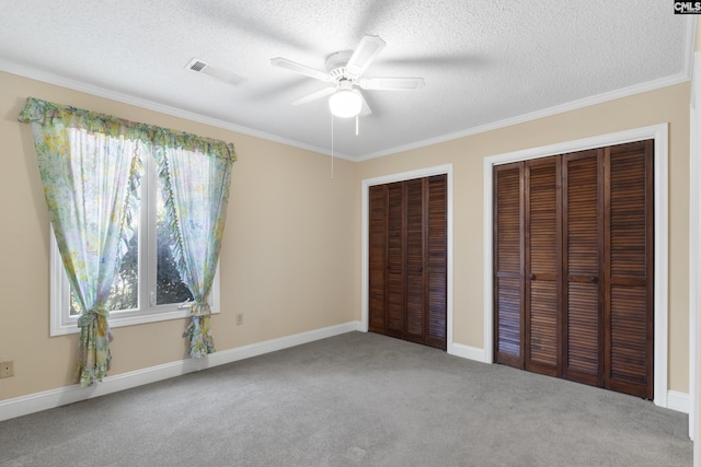 unfurnished bedroom featuring crown molding, two closets, a textured ceiling, and carpet