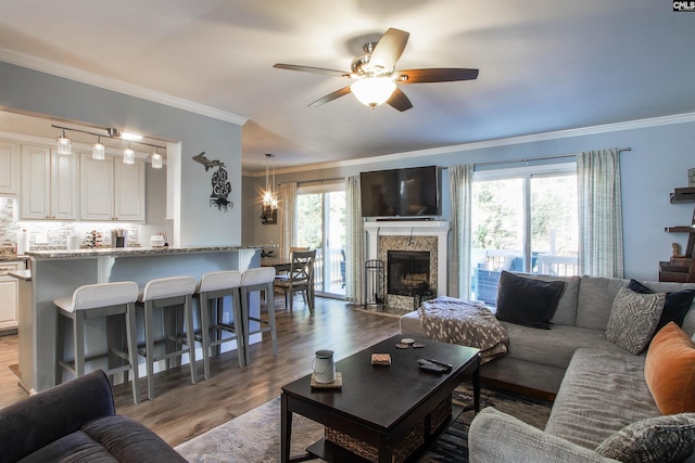 living room featuring crown molding, a stone fireplace, ceiling fan, and light wood-type flooring