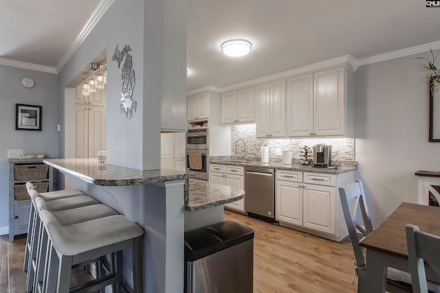 kitchen featuring sink, a breakfast bar area, stainless steel appliances, ornamental molding, and white cabinets