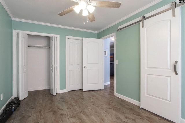 unfurnished bedroom featuring hardwood / wood-style floors, ceiling fan, multiple closets, crown molding, and a barn door