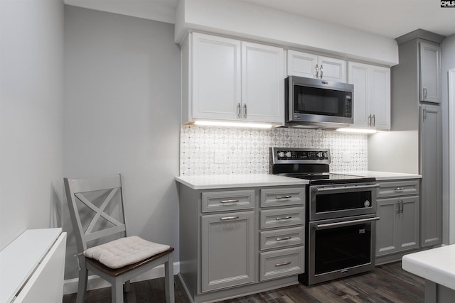 kitchen with appliances with stainless steel finishes, dark wood-type flooring, gray cabinetry, and decorative backsplash