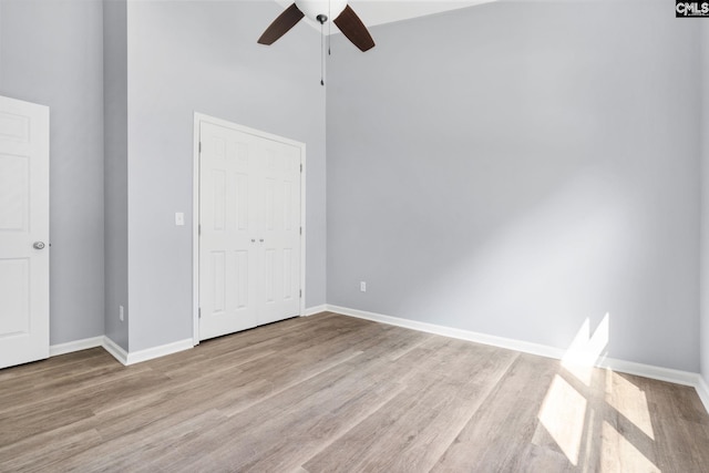 unfurnished bedroom featuring a towering ceiling, light hardwood / wood-style flooring, a closet, and ceiling fan