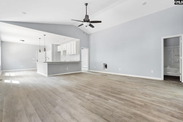 unfurnished living room with high vaulted ceiling, light wood-type flooring, sink, and ceiling fan