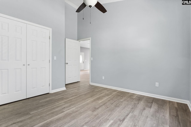 unfurnished bedroom with a high ceiling, a closet, ceiling fan, and light wood-type flooring