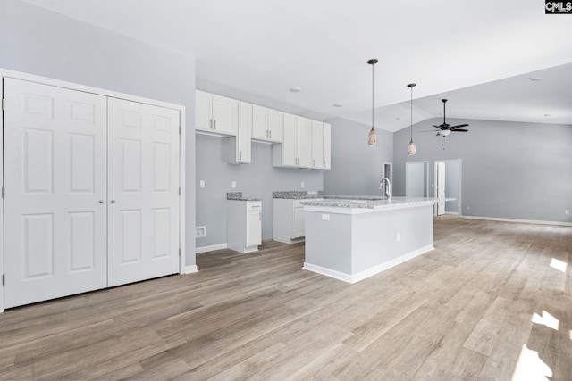 kitchen featuring ceiling fan, white cabinetry, light hardwood / wood-style floors, a center island with sink, and decorative light fixtures