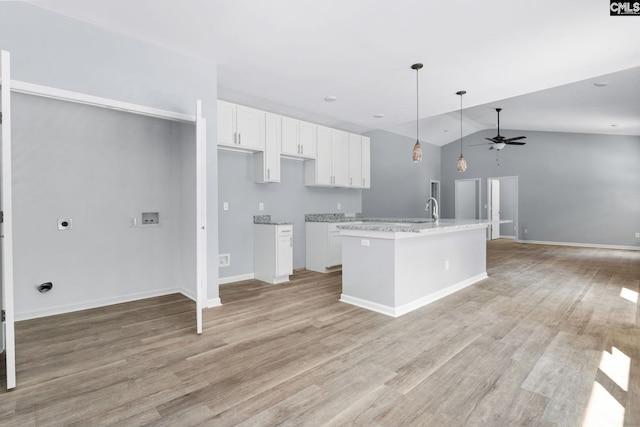 kitchen with white cabinetry, decorative light fixtures, light hardwood / wood-style flooring, light stone countertops, and a kitchen island with sink