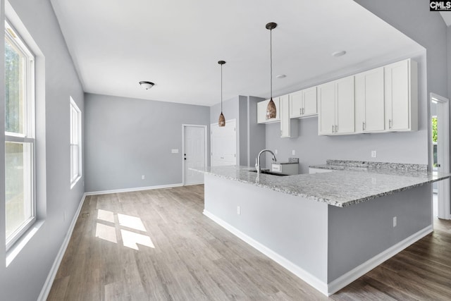 kitchen with sink, white cabinetry, light stone counters, decorative light fixtures, and a healthy amount of sunlight