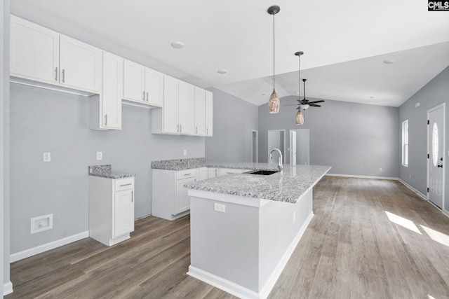 kitchen with sink, light stone counters, wood-type flooring, a kitchen island, and white cabinets