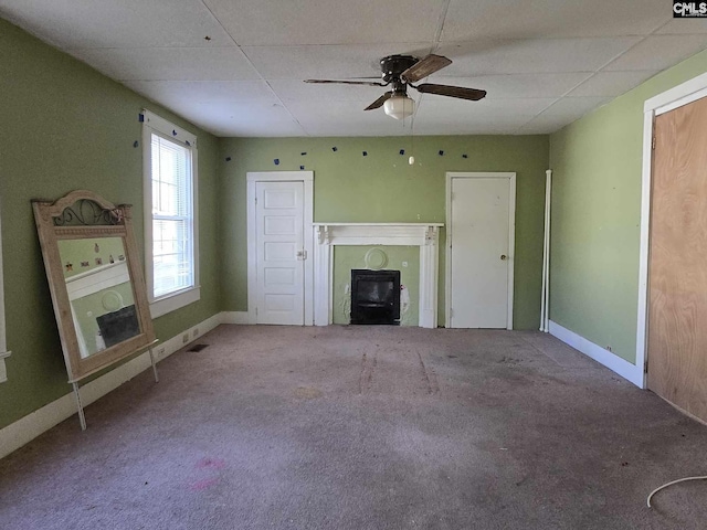 unfurnished living room featuring ceiling fan, a drop ceiling, carpet, and a wood stove