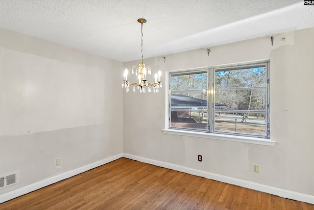 unfurnished room featuring wood-type flooring, a notable chandelier, and a textured ceiling