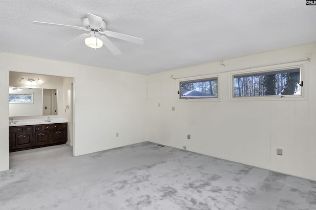 unfurnished bedroom with ensuite bath, sink, light colored carpet, ceiling fan, and a textured ceiling