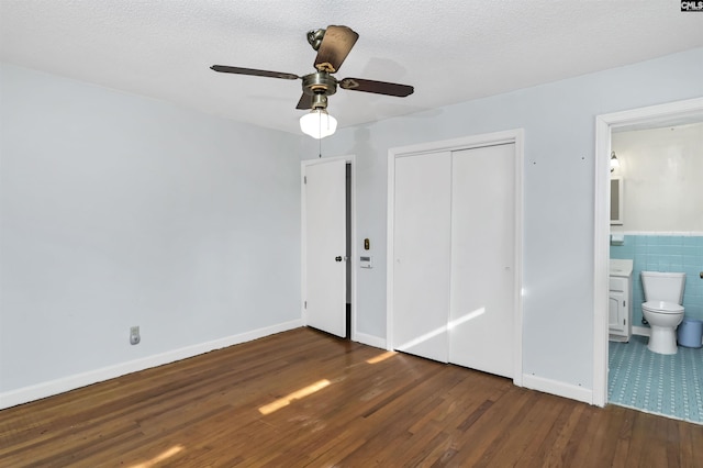 unfurnished bedroom with dark hardwood / wood-style flooring, a textured ceiling, a closet, and tile walls