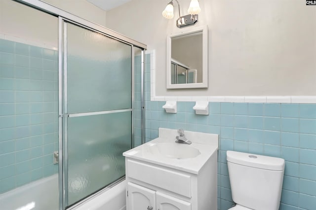 full bathroom featuring vanity, tile walls, toilet, and combined bath / shower with glass door