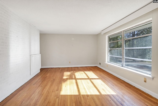 unfurnished room with brick wall, light hardwood / wood-style flooring, and a textured ceiling