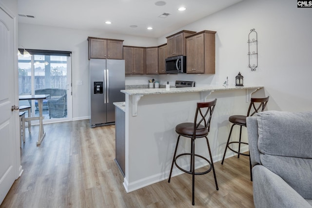 kitchen with light hardwood / wood-style flooring, stainless steel appliances, kitchen peninsula, and a kitchen bar