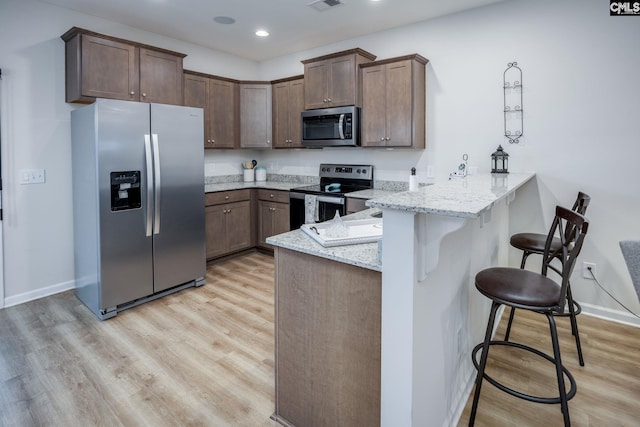 kitchen with appliances with stainless steel finishes, a kitchen breakfast bar, light stone counters, kitchen peninsula, and light wood-type flooring