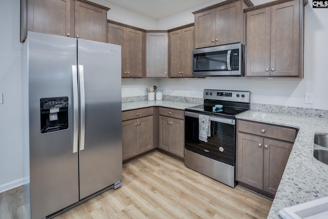 kitchen with light stone counters, stainless steel appliances, and light hardwood / wood-style flooring