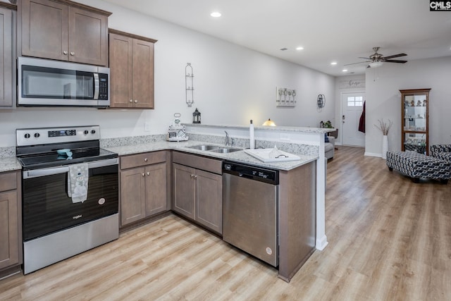 kitchen featuring sink, kitchen peninsula, stainless steel appliances, light stone countertops, and light wood-type flooring