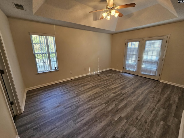 empty room with french doors, a textured ceiling, a tray ceiling, dark hardwood / wood-style flooring, and ceiling fan