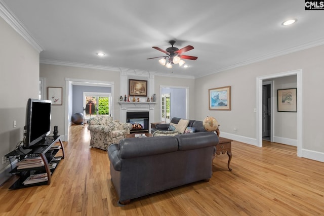 living room with crown molding, a large fireplace, ceiling fan, and light wood-type flooring