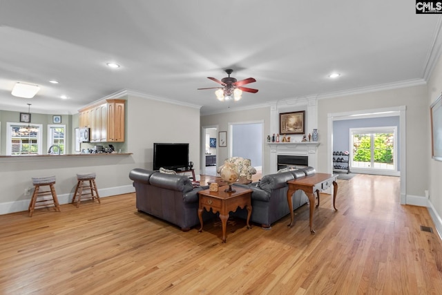 living room featuring light hardwood / wood-style flooring, crown molding, a fireplace, and ceiling fan with notable chandelier