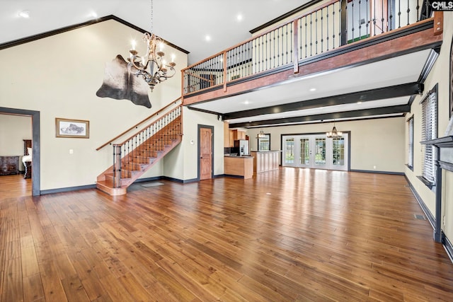 unfurnished living room with an inviting chandelier, beamed ceiling, hardwood / wood-style flooring, and a high ceiling