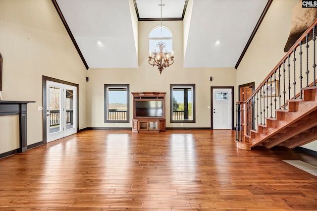 unfurnished living room featuring a notable chandelier, wood-type flooring, ornamental molding, and a high ceiling