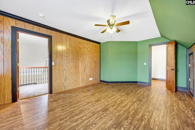 unfurnished room featuring wood-type flooring, wooden walls, ceiling fan, and vaulted ceiling